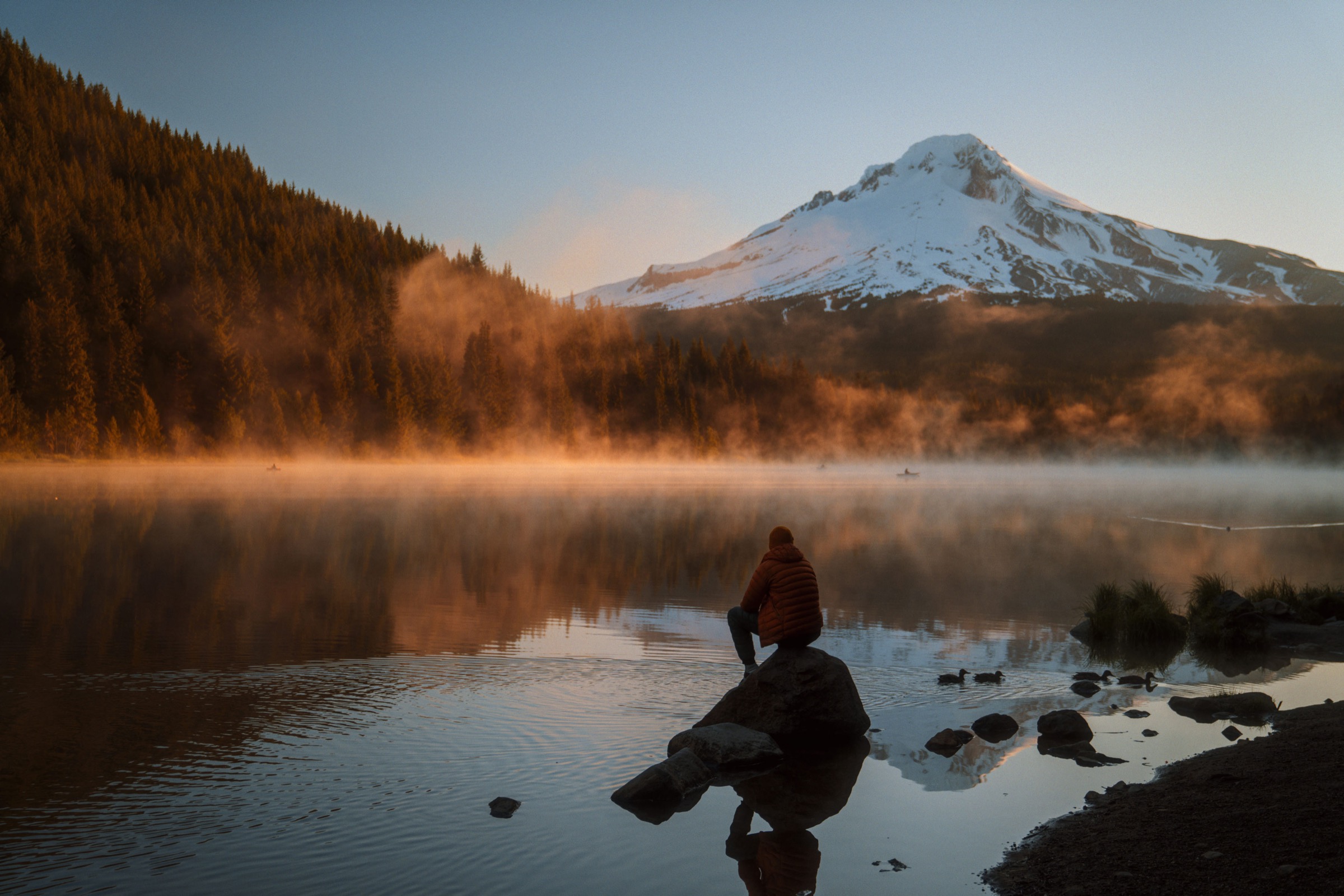 A figure on a rock at Trillium Lake below Mount Hood at sunrise